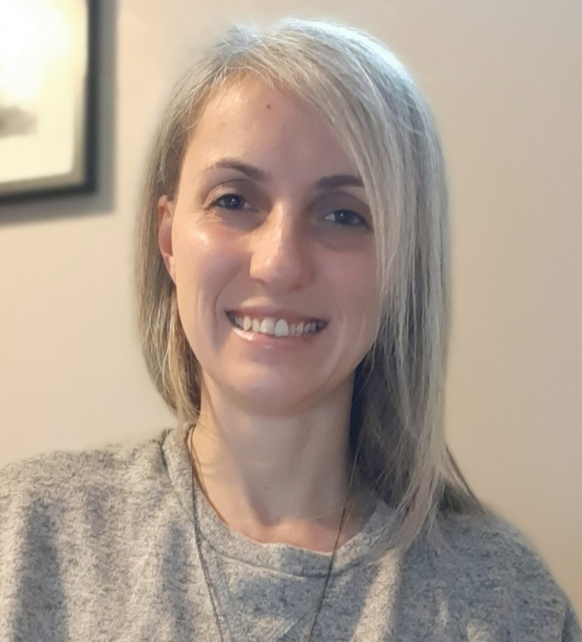 Project leader, Busra Yalcinoz-Ucan, wearing a gray sweater with a long silver necklace. She is looking and smiling at the camera.