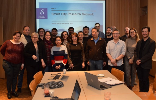19 forskere samlet foran storskjerm med smartby-presentasjon