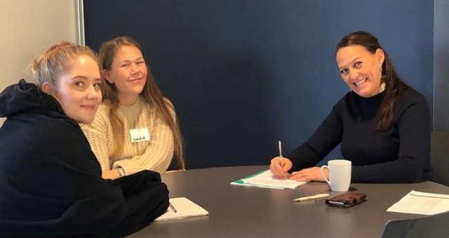 To studenter i samtale rundt et bord med en kvinnelig praksislærer