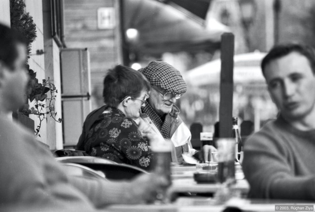 En eldre mann og dame leser avis på kafe.