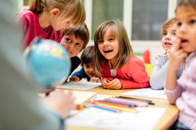 Barn smiler og ler rundt et bord i et klasserom