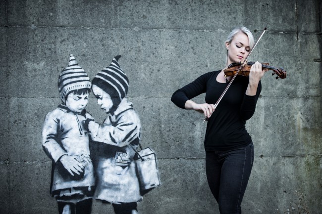 Kvinnelig fiolinist spiller i Stavanger sentrum foran grafitti