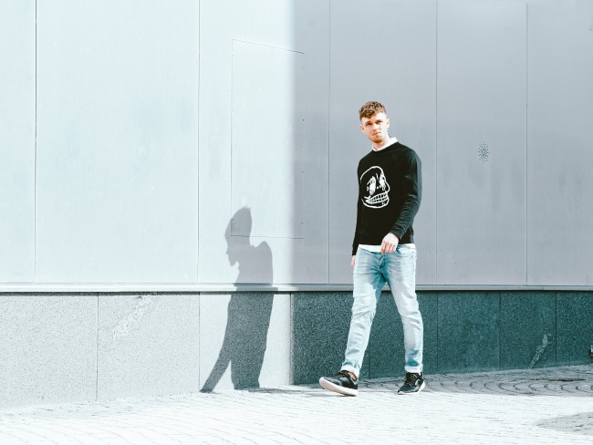 En ung mann kledd i jeans og svart genser går langs en vegg.