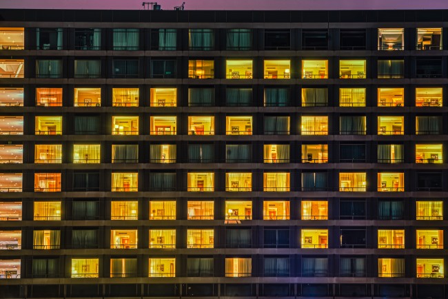 Building facade shows a windows and rooms pattern at night. The exterior features illuminated and dark living spaces with people living like neighbours in a shared communal space. Copenhagen, Denmark. Foto: Shutterstock