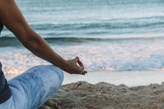 Deler av en person som sitter i meditasjonsstilling på en strand. 