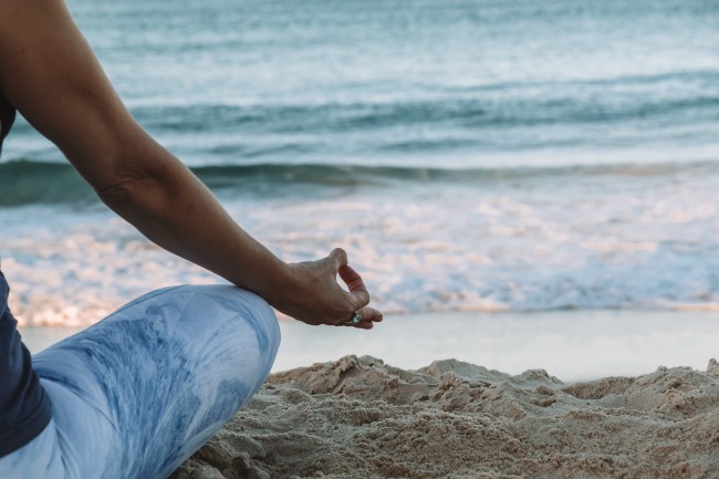Deler av en person som sitter i meditasjonsstilling på en strand.