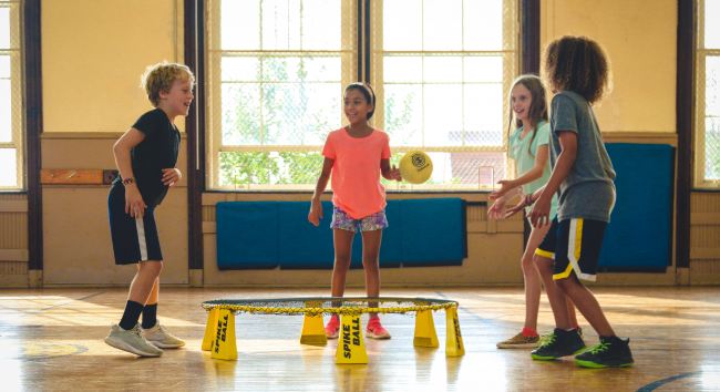 Fire barn leker med en gul ball inne i en gymsal