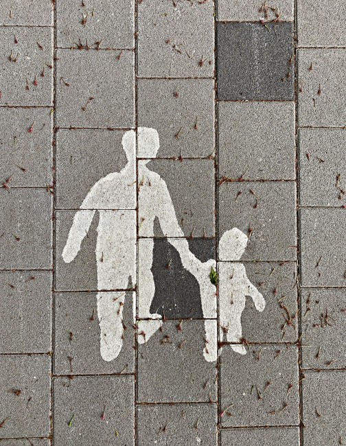 Figurer av voksen og barn som holder i hender malt i hvitt på grå asfalt