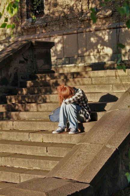 En kvinne sitter i en trapp med hodet i hendene.