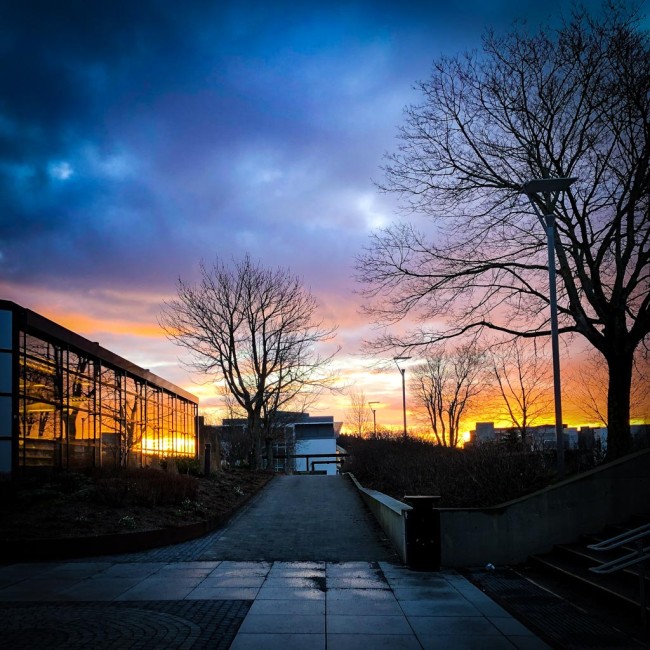 Gangvei ved siden av bygning med glassvindu hvor blå og oransje himmel i solnedgang reflekteres