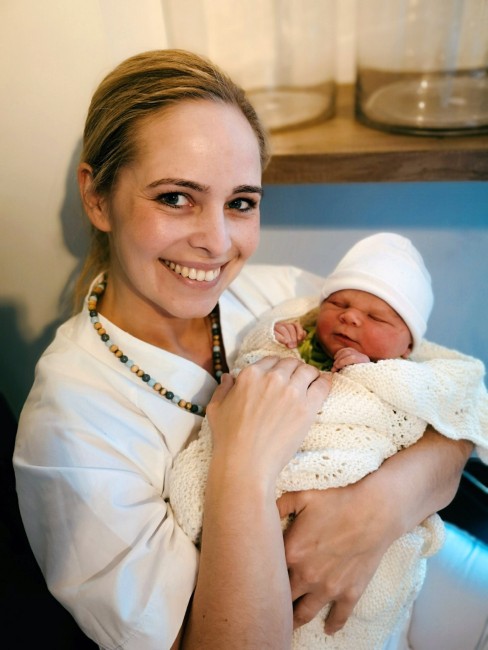 Bildet viser en tidligere masterstudent i jordmorfag som holder søsteren hennes sin nyfødte unge ikledd jordmor-uniform.