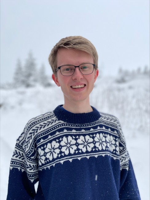 Ung mann med briller og ullgenser står utendørs med snø i håret