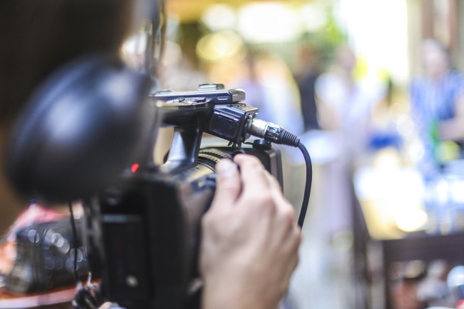 Delvis skjult person med filmkamera og headsett filmer skikkelser som er ute av fokus.