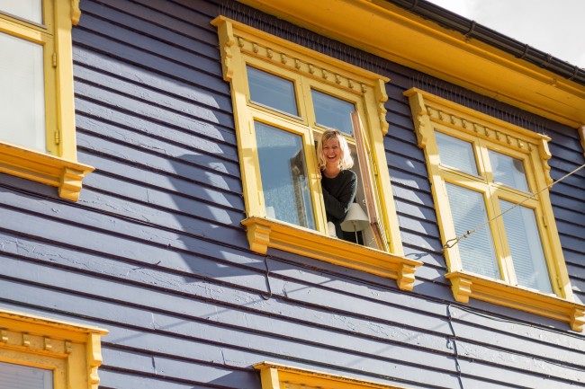 Ung kvinne titter ut av et vindu i et fargerikt trehus