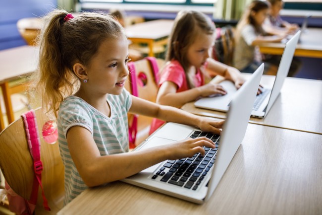 To jenter i barneskolealder sitter ved siden av hverandre og jobber på hver sin pc.