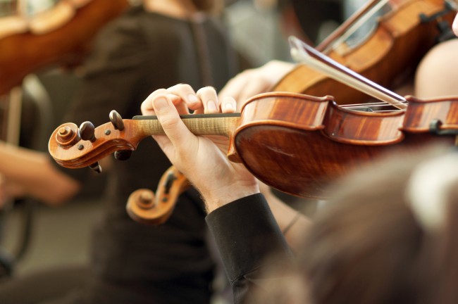 Bilde av hender som spiller fiolin i et orkester.