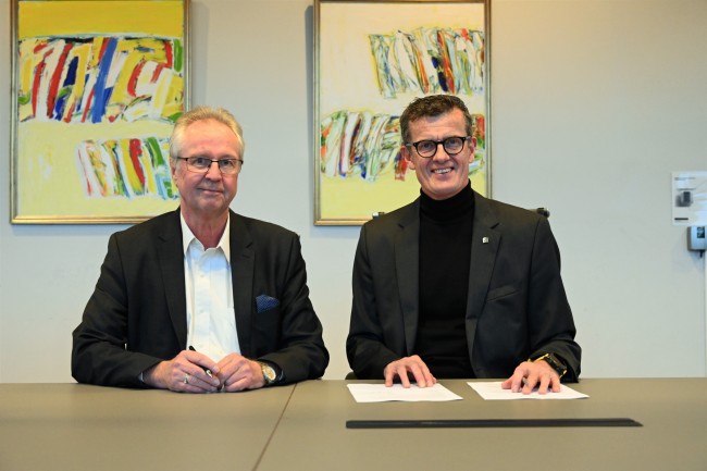To dresskledde menn signerer en avtale i et møterom