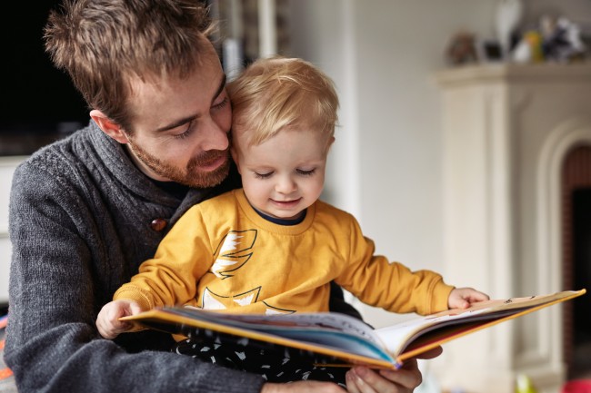 En voksen og et barn leser en bok i en stue.