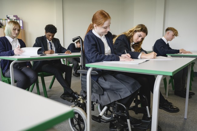 Elev i rullestol sitter ved pult i klasserom sammen med andre elever
