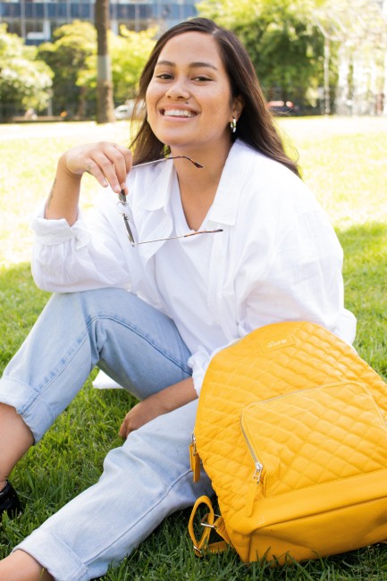 Ung kvinne med gul bag sitter på gressplen.
