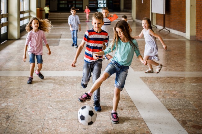 Fem barn spiller fotball i skolekorridor
