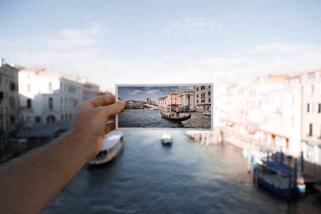 Hånd som holder et bilde av kanalen i Venezia foran kanalen i Venezia