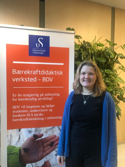 kvinne står foran plantevegg og en roll-up hvor det står "Bærekraftdidaktisk verksted"