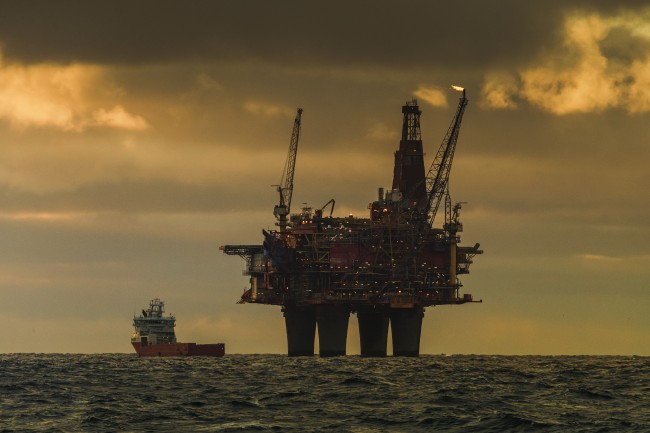 An oil platform in the North sea. A ship is beside it and the sky looks dark and ominous