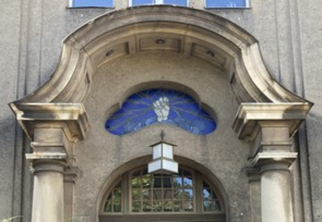 An ornate, stone doorway with blue stained glass above it. The glass has an image of a white fist holding lightning bolts.