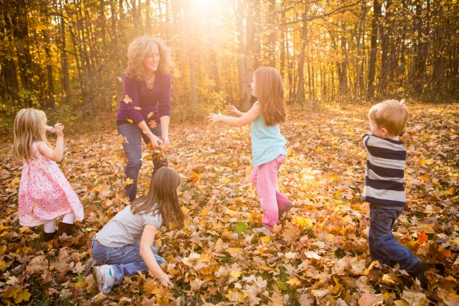 Mor og fire barn leker i vissent løv ved en skog.