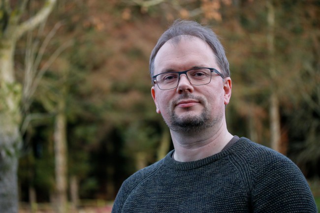 Finn Arne Jørgensen, mann med brillerm, utendørs med skog i bakgrunnen.