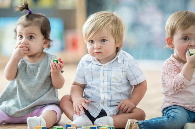 Tre småbarn sitter ved siden av hverandre på gulvet.
